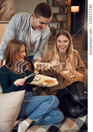 Man with women. Friends are sitting indoors at home and eating sushi together Man with women. Friends are sitting indoors at home and eating sushi together 126317146