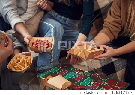 Friends are sitting indoors at home and eating together Friends are sitting indoors at home and eating together 126317150