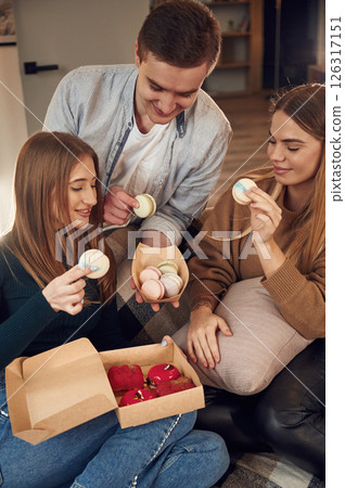 Friends are sitting indoors at home and eating macarons together 126317151