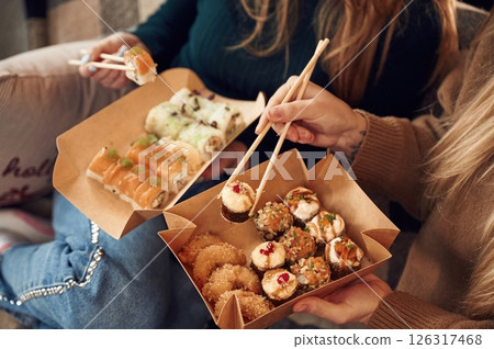 Two women are sitting and eating sushi indoors together Two women are sitting and eating sushi indoors together 126317468