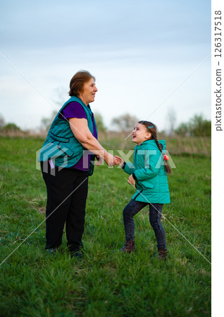 Grandmother and granddaughter sharing a joyful moment outdoors in a grassy field. 126317518