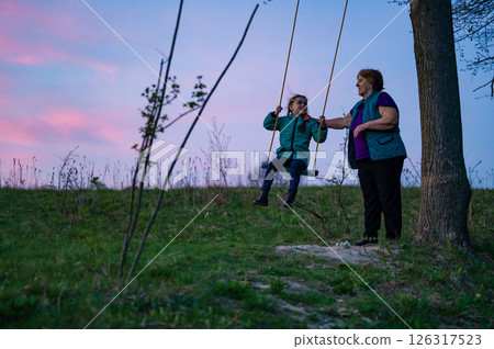 Grandmother and granddaughter enjoying a sunset swing ride. Grandmother and granddaughter enjoying a sunset swing ride. 126317523