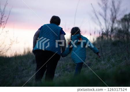 Grandmother and granddaughter walking together at sunset, holding hands. A heartwarming moment of family connection. Grandmother and granddaughter walking together at sunset, holding hands. A heartwarming moment of family connection. 126317524