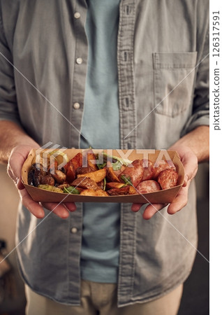 Close up view. Man in casual clothes is holding food that are in the paper eco box. Potatoes, sausages, mushrooms, zucchini 126317591