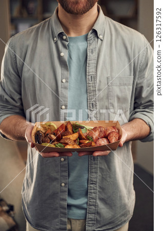 Close up view. Man in casual clothes is holding food that are in the paper eco box. Potatoes, sausages, mushrooms, zucchini Close up view. Man in casual clothes is holding food that are in the paper eco box. Potatoes, sausages, mushrooms, zucchini 126317592