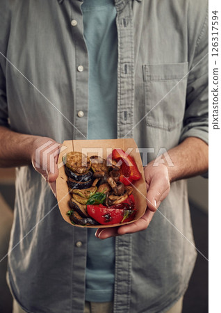 Close up view. Man in casual clothes is holding food that are in the paper eco box. Potatoes, sausages, mushrooms, zucchini Close up view. Man in casual clothes is holding food that are in the paper eco box. Potatoes, sausages, mushrooms, zucchini 126317594