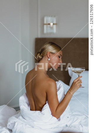 Close-up portrait of a seductive young bride with a glass of champagne, wrapped in a white blanket Close-up portrait of a seductive young bride with a glass of champagne, wrapped in a white blanket 126317606