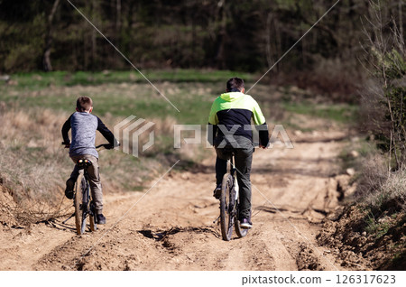 Father and son enjoy a bike ride on a sunny day, traversing a sandy trail through nature. 126317623