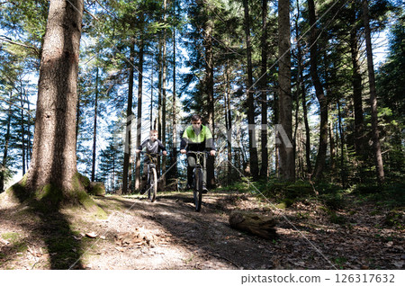 Two mountain bikers ride a trail through a sun-dappled forest. A fun outdoor adventure. 126317632