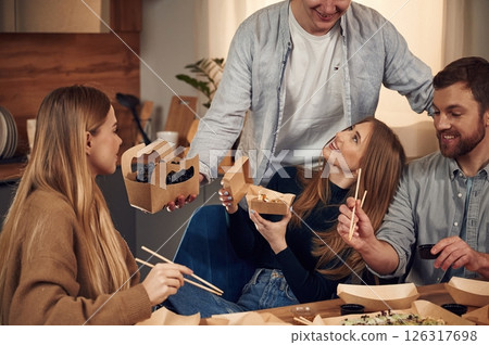 Casual conversation. Friends are sitting indoors at home and eating sushi together Casual conversation. Friends are sitting indoors at home and eating sushi together 126317698