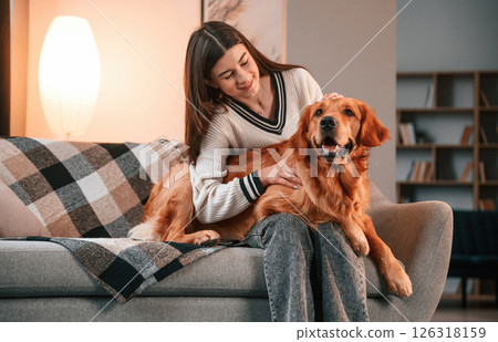 On the sofa together. Cute golden retriever is in domestic room with his owner, beautiful young woman 126318159