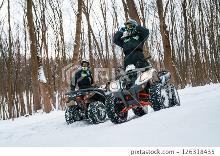 Wearing the protective glasses. Two people are riding ATV in the winter forest Wearing the protective glasses. Two people are riding ATV in the winter forest 126318435