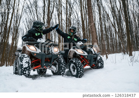 Making high five. Two people are riding ATV in the winter forest 126318437