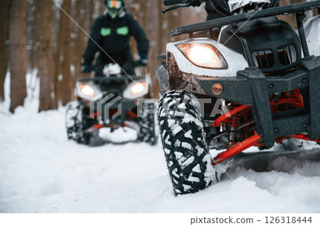 On the snowy ground. Two people are riding ATV in the winter forest 126318444