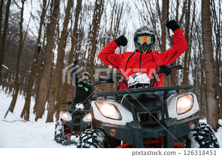 On the snowy ground. Two people are riding ATV in the winter forest On the snowy ground. Two people are riding ATV in the winter forest 126318451