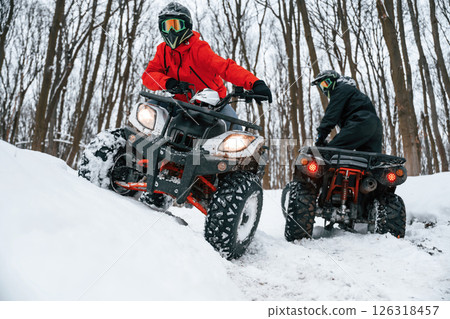 On the off road. Two people are riding ATV in the winter forest On the off road. Two people are riding ATV in the winter forest 126318457