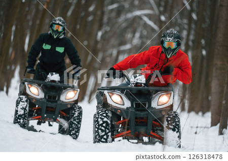Conception of active recreation. Two people are riding ATV in the winter forest Conception of active recreation. Two people are riding ATV in the winter forest 126318478