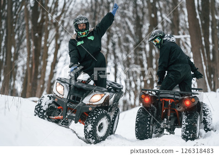 Riding the opposite ways. Two people are on the ATV in the winter forest 126318483