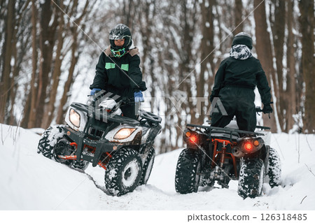 Riding the opposite ways. Two people are on the ATV in the winter forest Riding the opposite ways. Two people are on the ATV in the winter forest 126318485