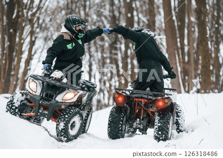 Making gestures. Two people are riding ATV in the winter forest Making gestures. Two people are riding ATV in the winter forest 126318486