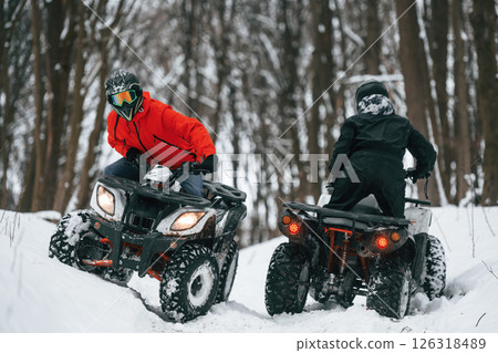 Riding the opposite ways. Two people are on the ATV in the winter forest Riding the opposite ways. Two people are on the ATV in the winter forest 126318489