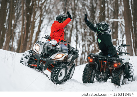Making high five. Two people are riding ATV in the winter forest Making high five. Two people are riding ATV in the winter forest 126318494
