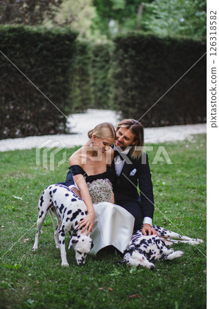 Stylish young beautiful newlywed couple walking at wedding in park with two dalmatians Stylish young beautiful newlywed couple walking at wedding in park with two dalmatians 126318582