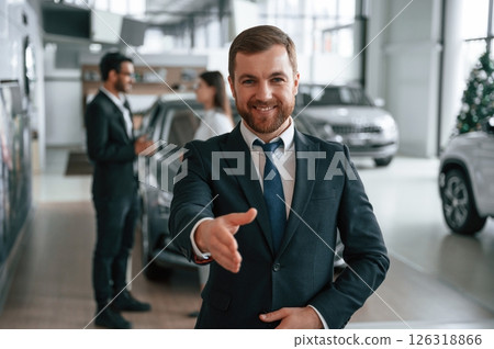 Handsome man is standing in front of his coworkers. Three people are together in the car showroom 126318866
