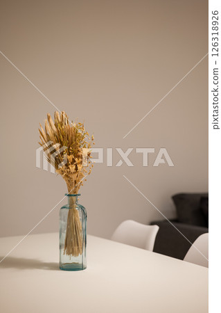 Side angle of dining table with white chairs and blue vase centerpiece holding dried floral bouquet 126318926