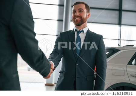 Two businessmen are standing in the car showroom and making a deal, handshake Two businessmen are standing in the car showroom and making a deal, handshake 126318931