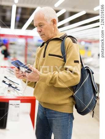 Elderly man examines tablet computer in showroom of electronics store 126319166