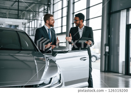 Standing and talking near automobile. Man is consulting the customer in the car showroom Standing and talking near automobile. Man is consulting the customer in the car showroom 126319200