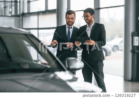 Near grey colored automobile. Two businessmen are working together in the car showroom Near grey colored automobile. Two businessmen are working together in the car showroom 126319227