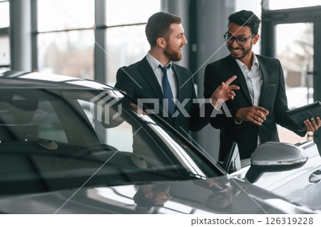 Near grey colored automobile. Two businessmen are working together in the car showroom Near grey colored automobile. Two businessmen are working together in the car showroom 126319228