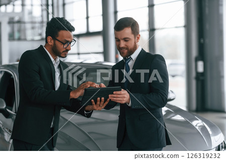 New plan. Standing near automobile with graphic tablet. Two businessmen are working together in the car showroom 126319232