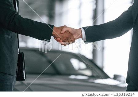 Close up view. Two businessmen are standing in the car showroom and making a deal, handshake Close up view. Two businessmen are standing in the car showroom and making a deal, handshake 126319234