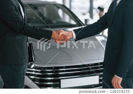 Close up view. Two businessmen are standing in the car showroom and making a deal, handshake 126319235