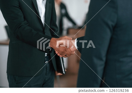 Close up view. Two businessmen are standing in the car showroom and making a deal, handshake Close up view. Two businessmen are standing in the car showroom and making a deal, handshake 126319236