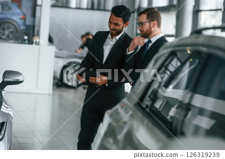 New plan. Standing near automobile with graphic tablet. Two businessmen are working together in the car showroom New plan. Standing near automobile with graphic tablet. Two businessmen are working together in the car showroom 126319239