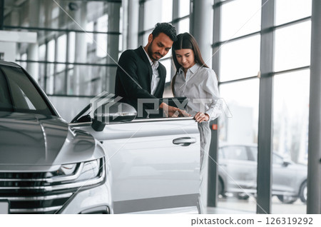 Man in formal clothes is consulting woman about the automobile in the car dealership Man in formal clothes is consulting woman about the automobile in the car dealership 126319292