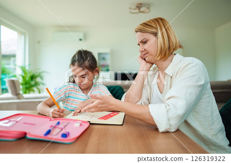 Mother helps daughter with homework in cozy living room Mother helps daughter with homework in cozy living room 126319322