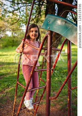 Joyful girl climbing on playground equipment in sunny park 126319396
