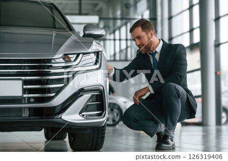 Man in suit and tie is sitting and checking quality of the vehicle in the car showroom 126319406