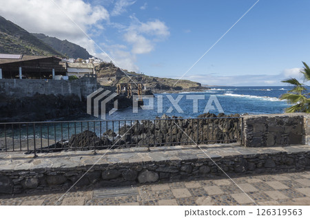 Old fish factory building at center of Garachico old town with sea pools and lava rocks at Tenerife canary island, Spain. Blue sky white clouds background 126319563