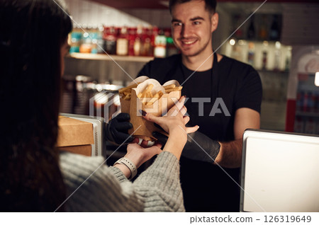 Worker is serving woman by giving her set of French fries that is in the paper eco boxes Worker is serving woman by giving her set of French fries that is in the paper eco boxes 126319649