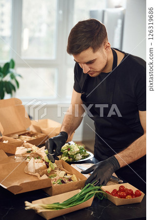 Adding vegetables to the burger. Man is packing food into the paper eco boxes. Indoors, restaurant 126319686