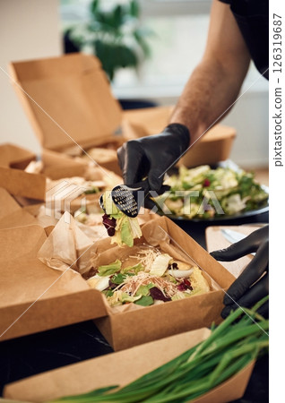 Adding vegetables to the burger. Man is packing food into the paper eco boxes. Indoors, restaurant Adding vegetables to the burger. Man is packing food into the paper eco boxes. Indoors, restaurant 126319687