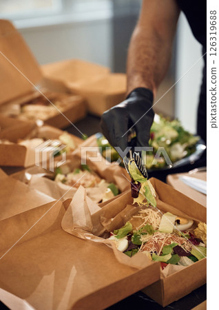 Close up view. Burgers and vegetables. Man is packing food into the paper eco boxes. Indoors, restaurant 126319688