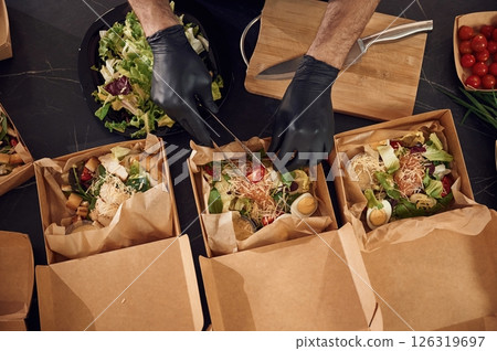 Delicious meal. Man is packing food into the paper eco boxes. Indoors, restaurant 126319697