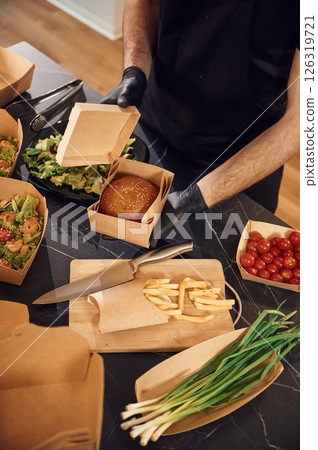 Opening the box with burger. Man is packing food. Indoors, restaurant Opening the box with burger. Man is packing food. Indoors, restaurant 126319721